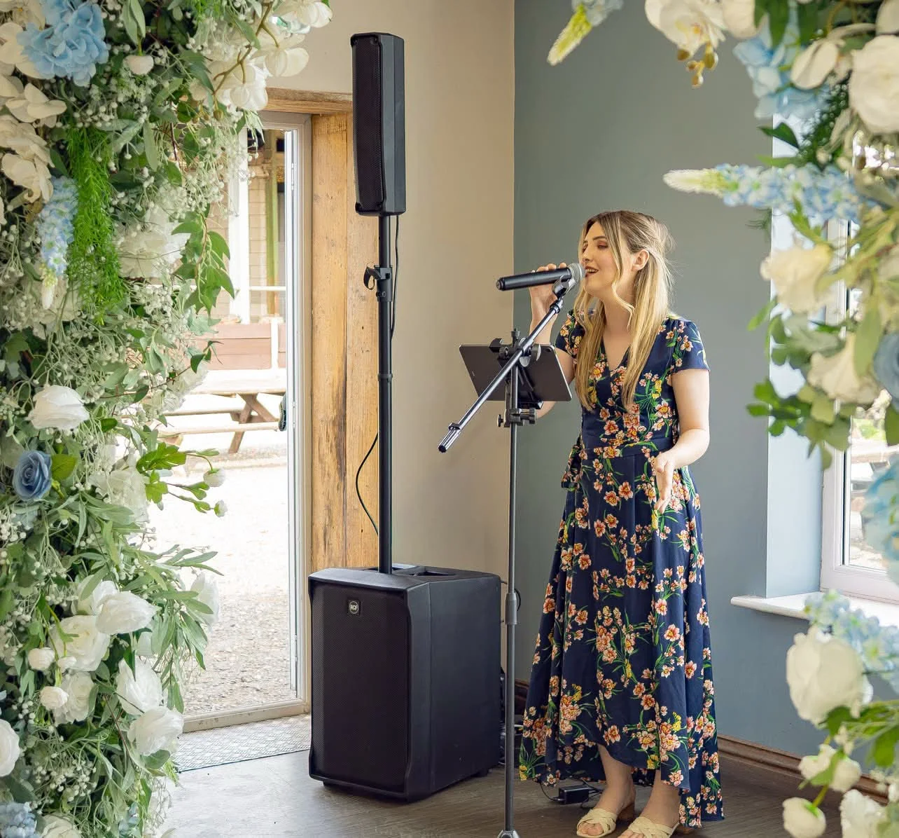 Jenny Jones singing live at a wedding beside a floral arch